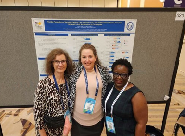 Two medical faculty members and a student at a conference standing in front of an educational exhibit.